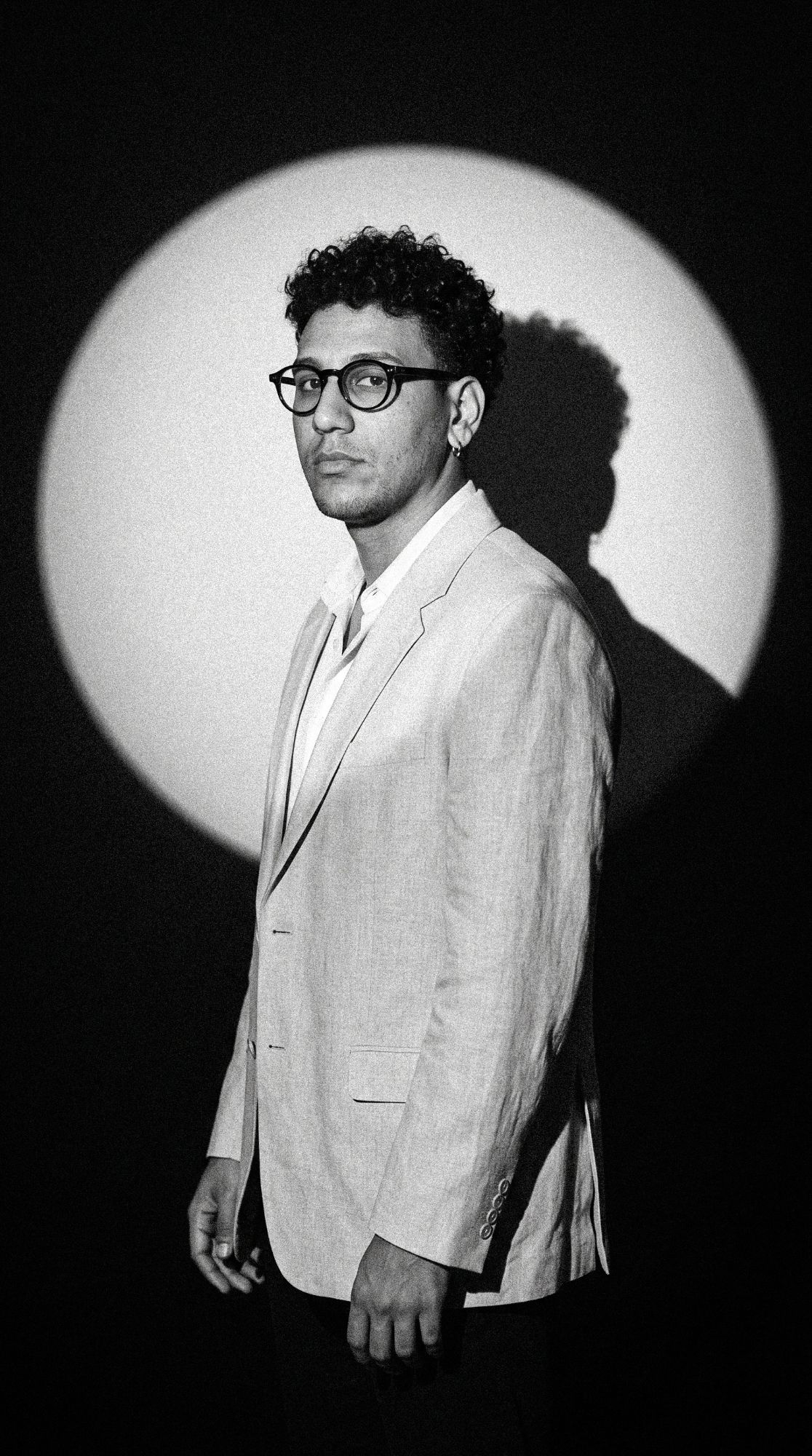 Caique Colman in a light suit, under a circle of light